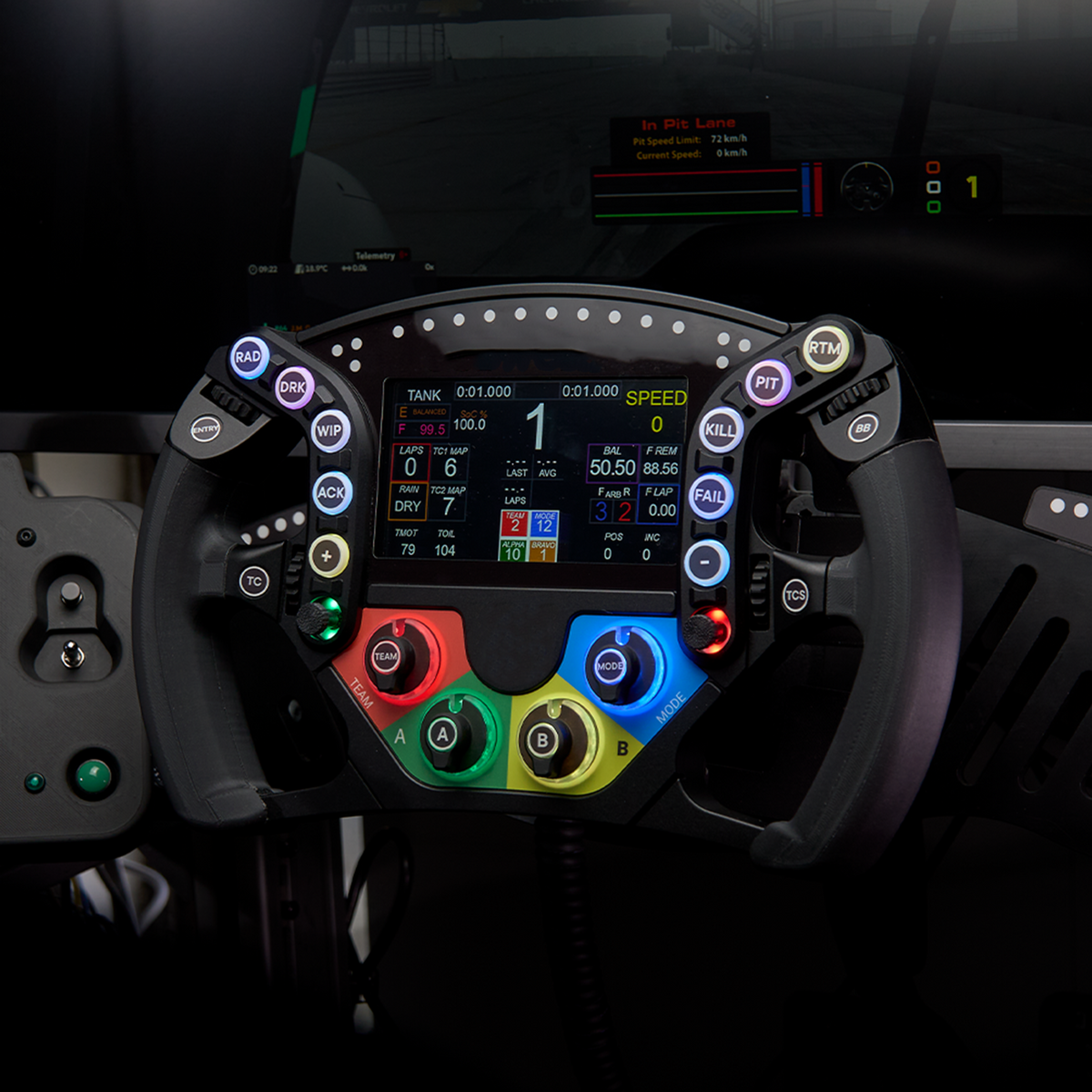 A close-up of a racing steering wheel with a large illuminated digital display in the center and multiple colored control buttons around the rim, photographed in a dark cockpit environment.